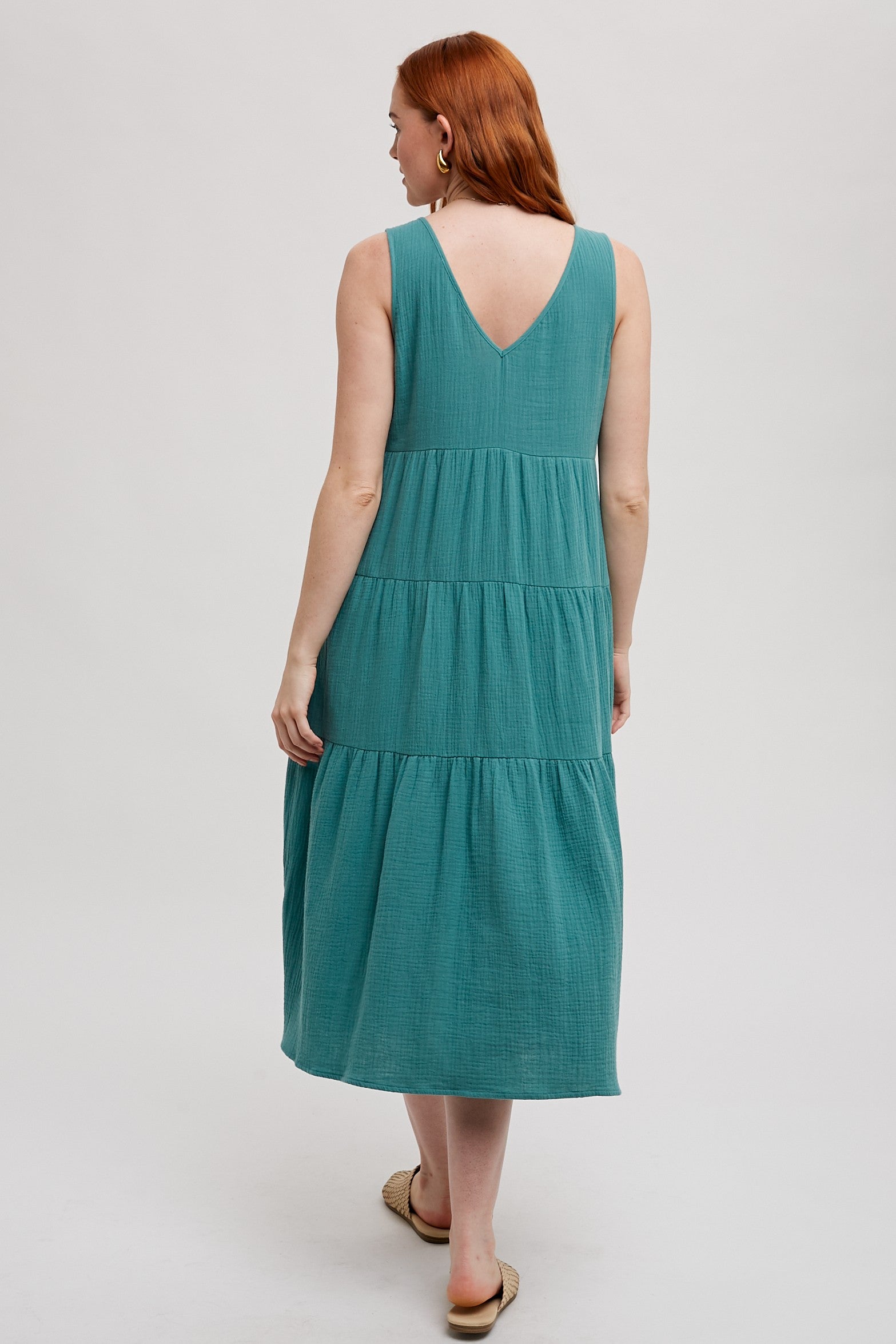 Back view of a woman wearing a sea green tank tiered dress on a white background