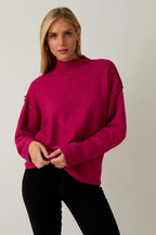 Woman wearing a berry mock neck sweater against a plain background
