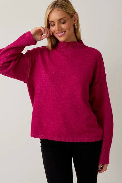 Woman wearing a berry mock neck sweater against a plain background