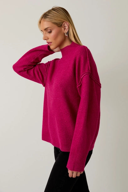 Woman wearing a berry mock neck sweater against a plain background