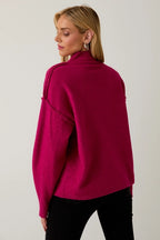 Woman wearing a berry mock neck sweater against a plain background