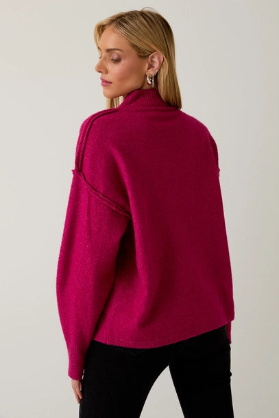 Woman wearing a berry mock neck sweater against a plain background