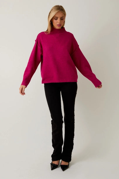 Woman wearing a berry mock neck sweater against a plain background