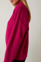 Woman wearing a berry mock neck sweater against a plain background