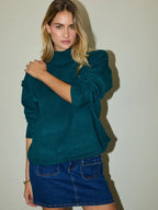 Woman wearing a hunter green sweater and blue denim skirt against a plain background