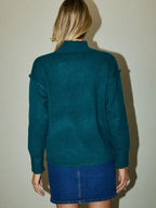 Back view of woman wearing a hunter green sweater and blue denim skirt against a plain background