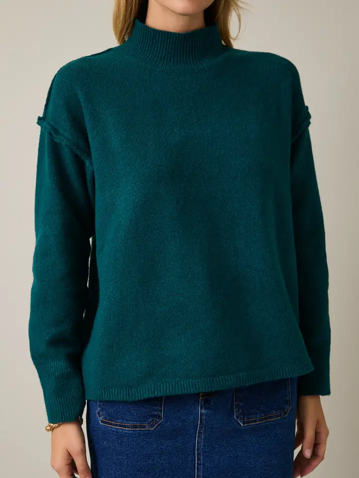 Woman wearing a hunter green sweater and blue denim skirt against a plain background
