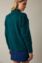 Back view of woman wearing a hunter green sweater and blue denim skirt against a plain background