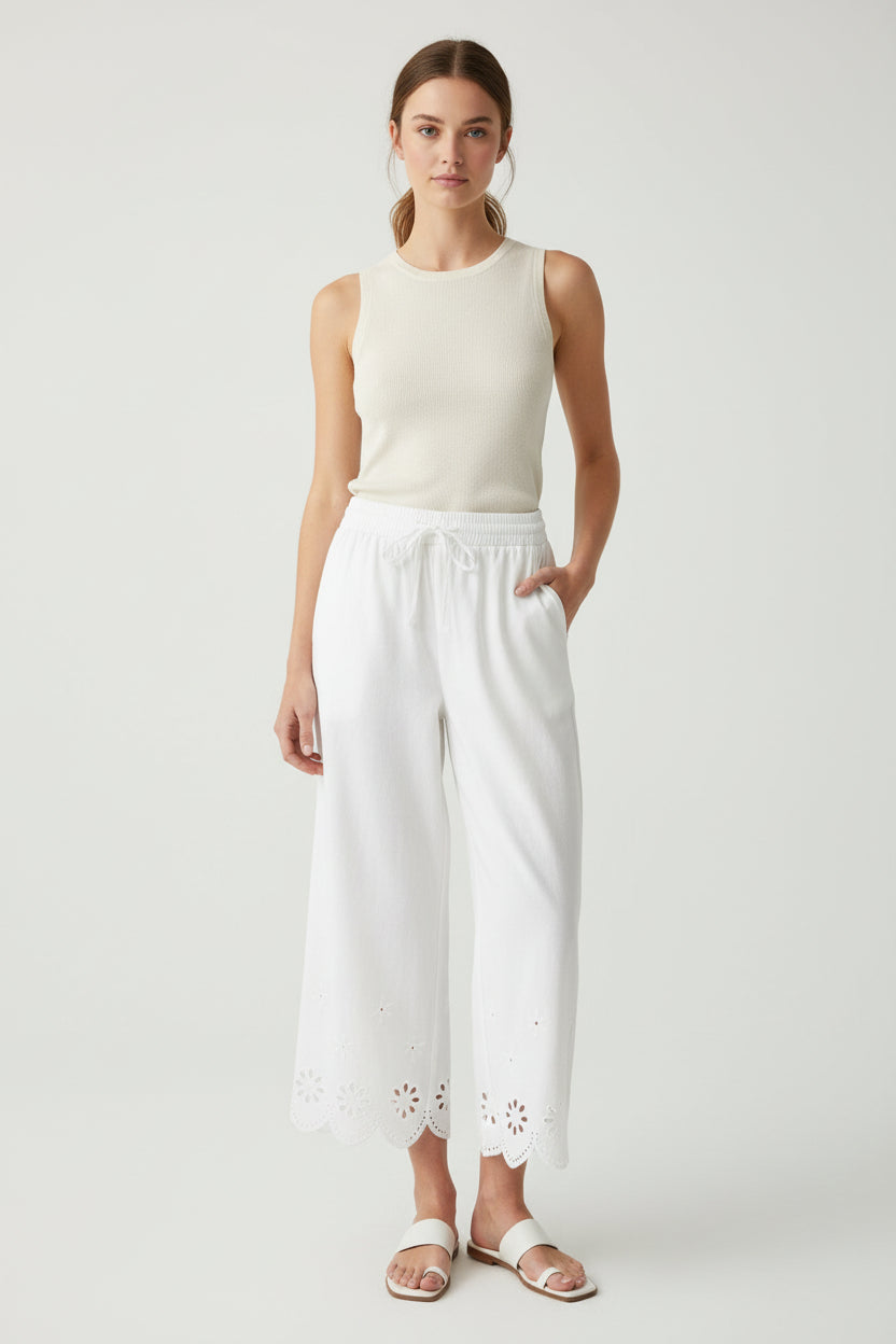 Woman wearing a white sleeveless top and wide-leg cut out detail crop pants on a plain background