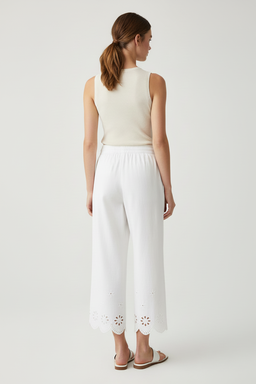Back view of a woman wearing a white sleeveless top and wide-leg cut out detail crop pants on a plain background