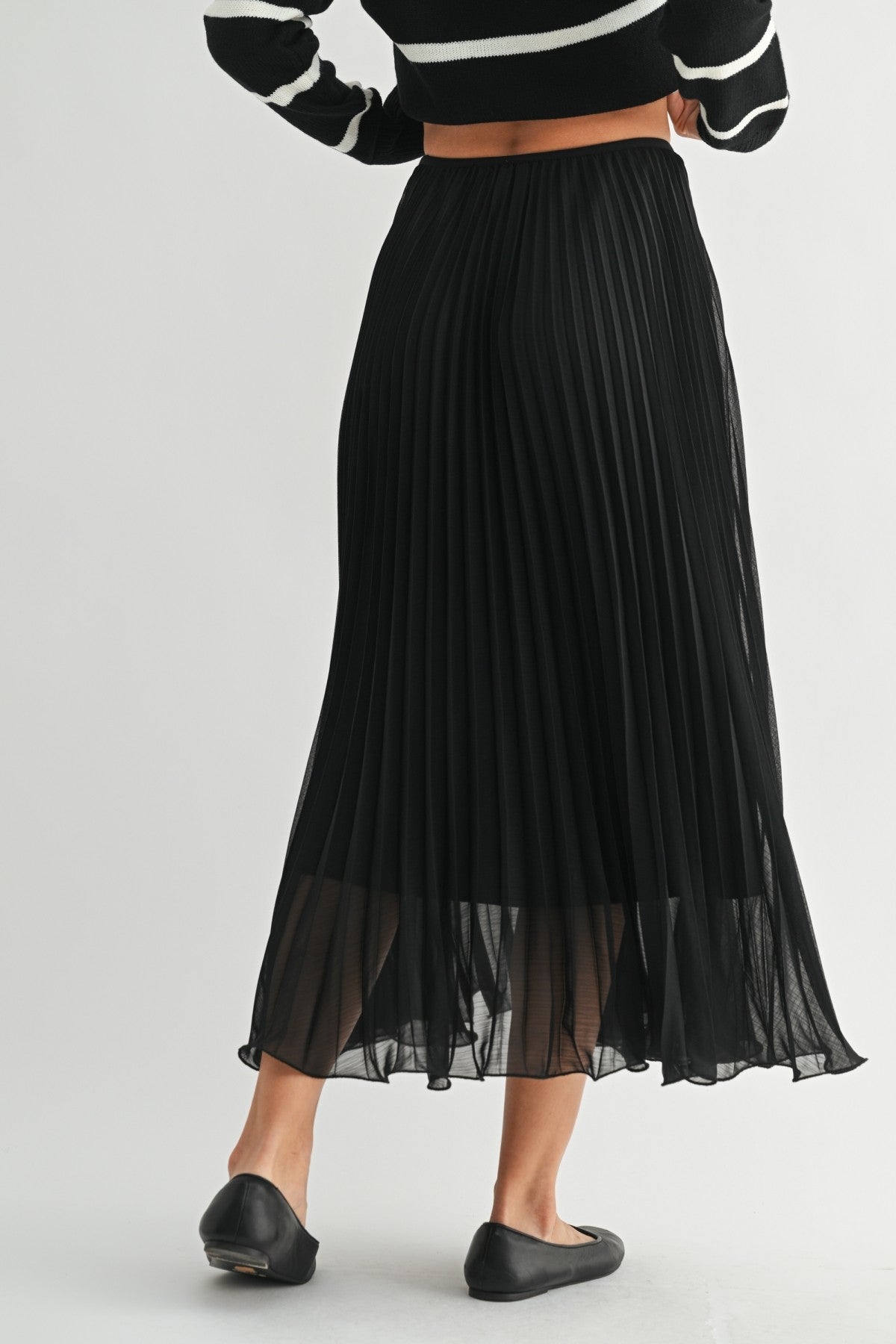 Back view of a woman wearing a black chiffon pleated midi skirt on a white background