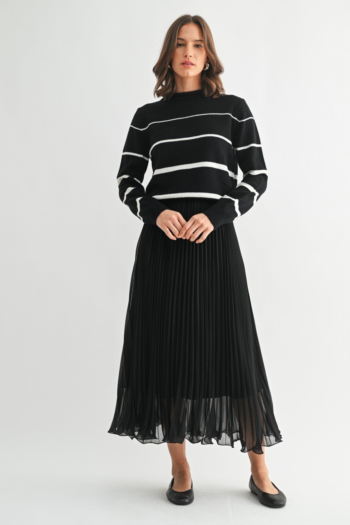 Woman wearing a black chiffon pleated midi skirt and sweater on a white background