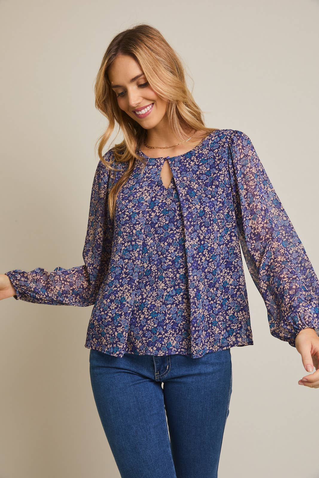 Woman wearing a floral button pleated top and jeans against a gray background