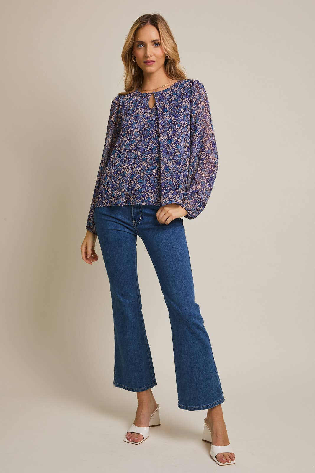 Woman wearing a floral button pleated top and jeans against a gray background