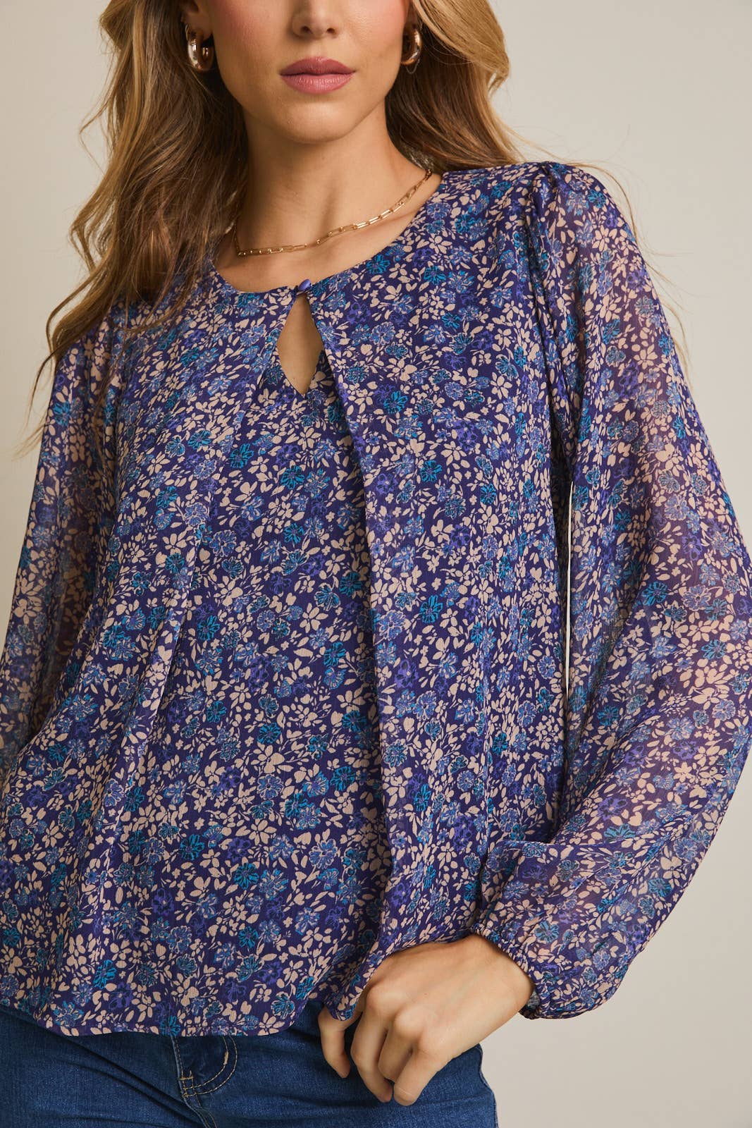 Woman wearing a floral button pleated top and jeans against a gray background