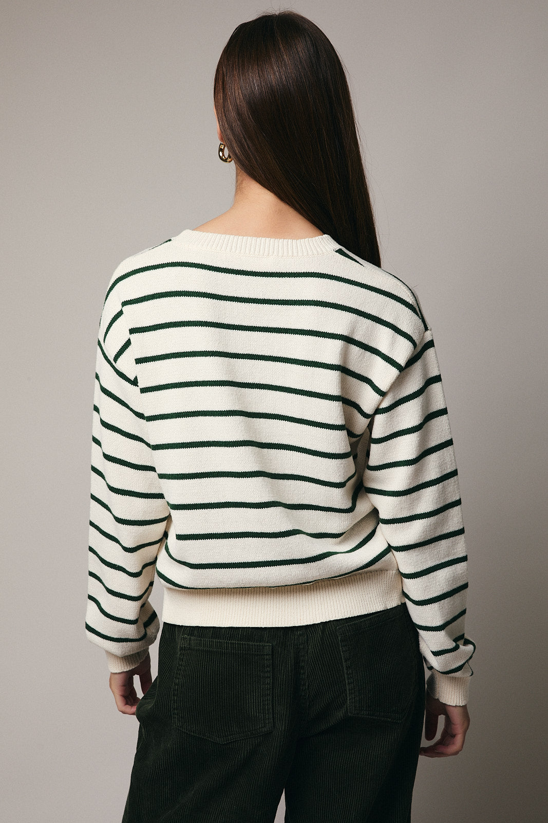 Back viewe of woman wearing green and cream striped sweater on gray background