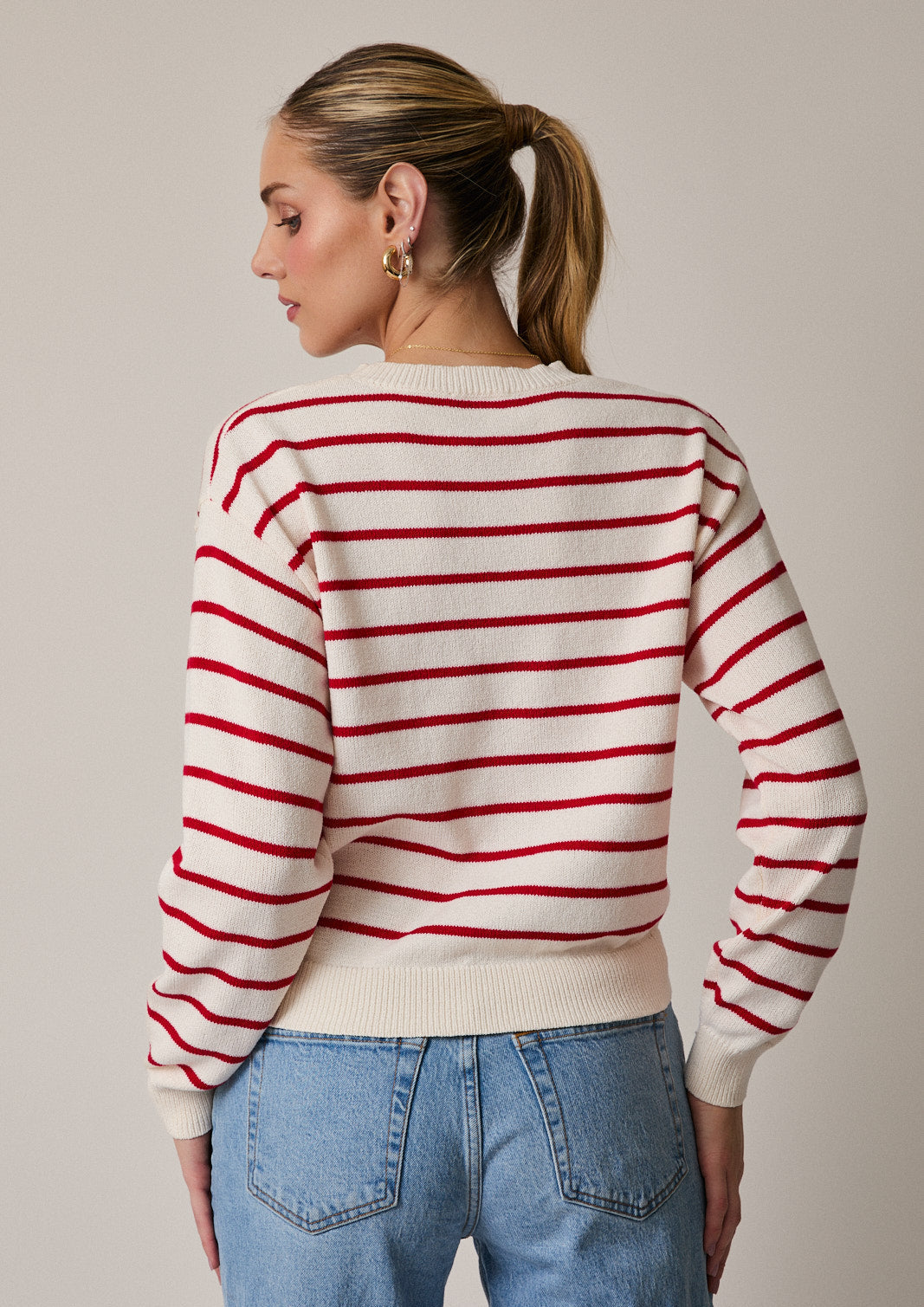 Back view of woman wearing red and cream striped sweater on gray background