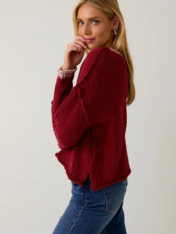Woman wearing a berry sweater with cream contrast trim on a plain background