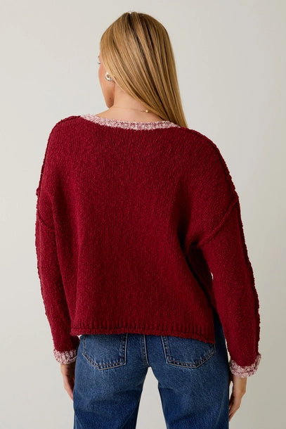 Woman wearing a berry sweater with cream contrast trim on a plain background