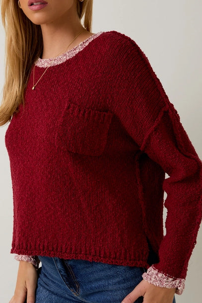Woman wearing a berry sweater with cream contrast trim on a plain background