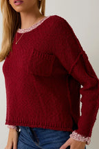 Woman wearing a berry sweater with cream contrast trim on a plain background
