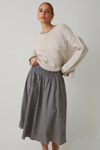 Woman wearing a textured light grey sweater with black contrast trim and skirt on a plain background