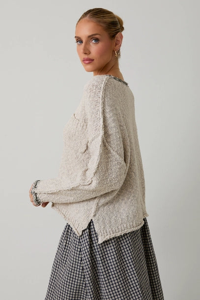 Woman wearing a textured light grey sweater with black contrast trim on a plain background