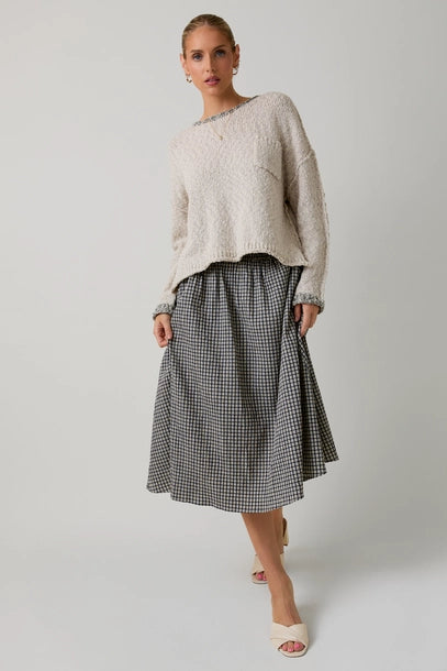 Woman wearing a textured light grey sweater with black contrast trim and skirt on a plain background