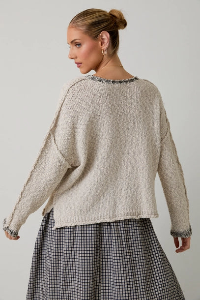 Back view of a woman wearing a textured light grey sweater with black contrast trim on a plain background